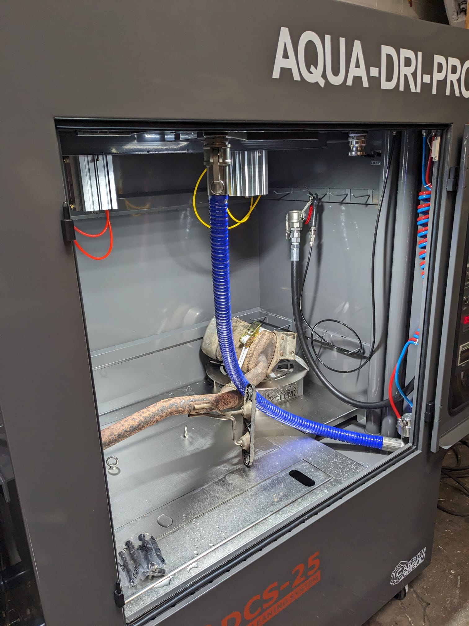 The image shows a machine labeled "AQUA-DRI-PRO" with internal components, including a rusted metal piece, hoses, and wires inside.
